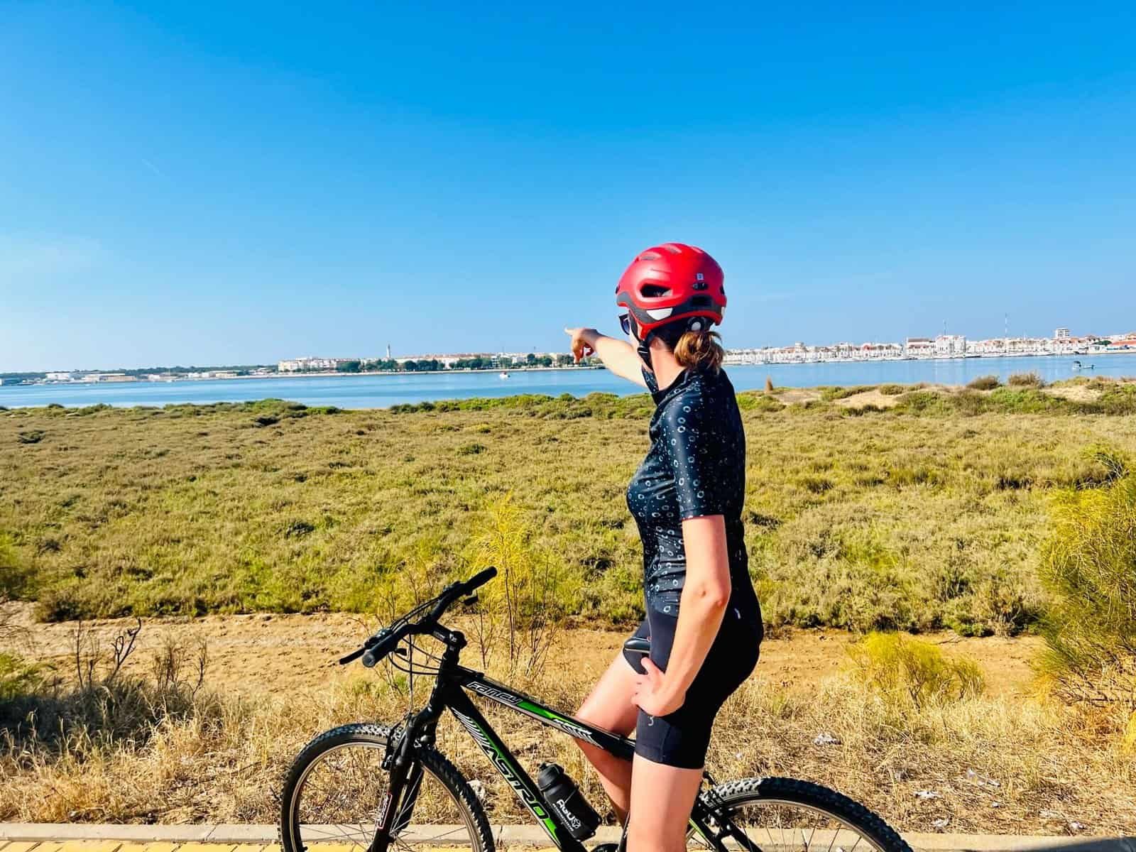 Fietser met helm wijst naar horizon bij de kustlijn.