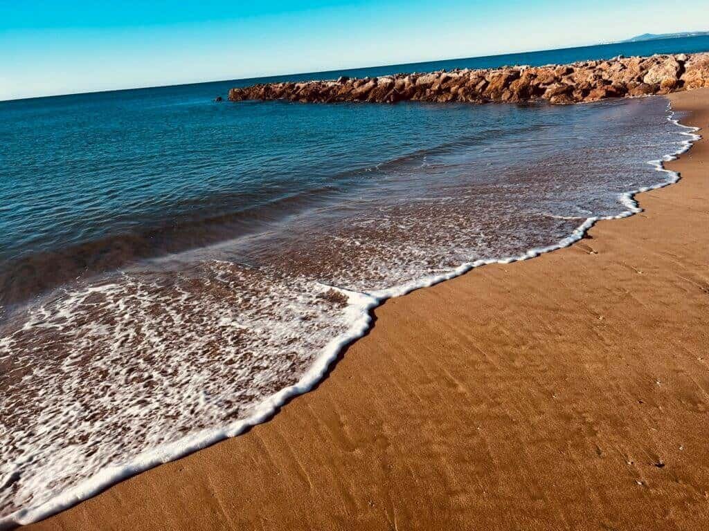 Scenic beach scene with calm waves, sandy shore, and rocky breakwater, perfect for relaxing seaside.