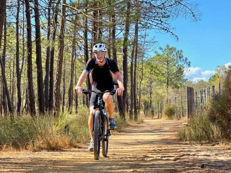 Fietser met helm op gravelpad in bosrijke omgeving.