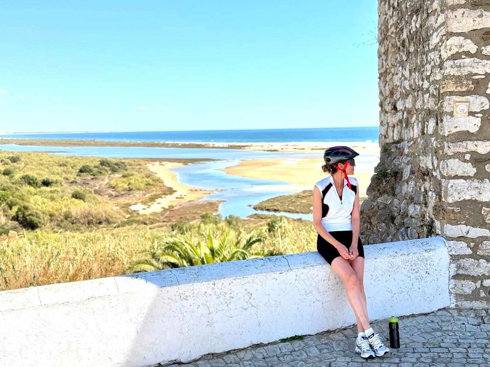 Cyclist resting by historic stone wall overlooking the coast.
