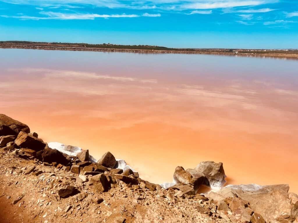 Salt lake reflecting vibrant sunset colours, surrounded by rocky terrain.