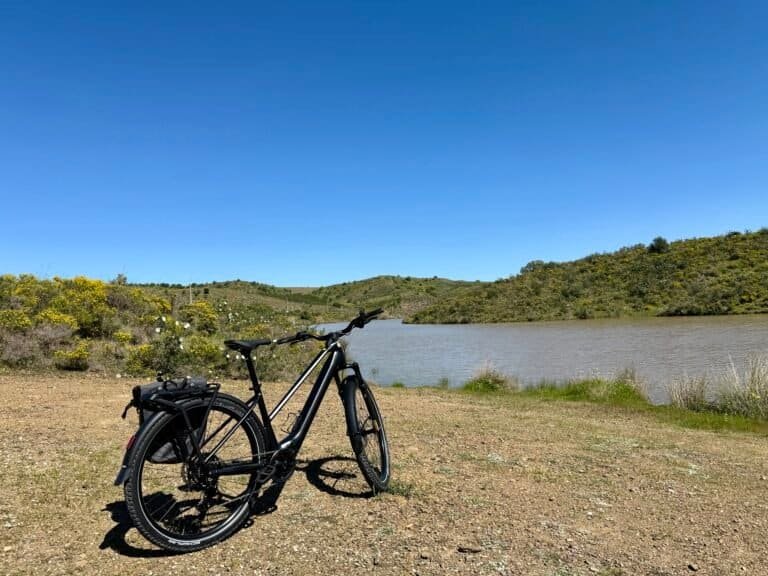 Algarve cycling rides: Bicycle parked near a lake with lush hills in the background.