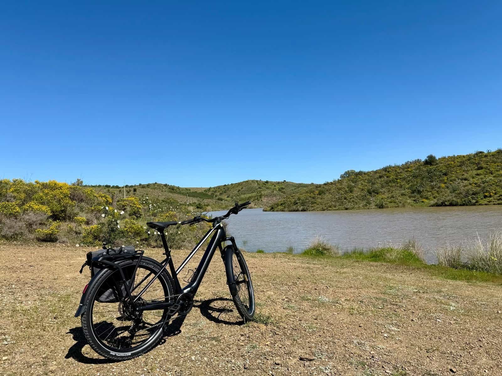 Algarve cycling rides: Bicycle parked near a lake with lush hills in the background.