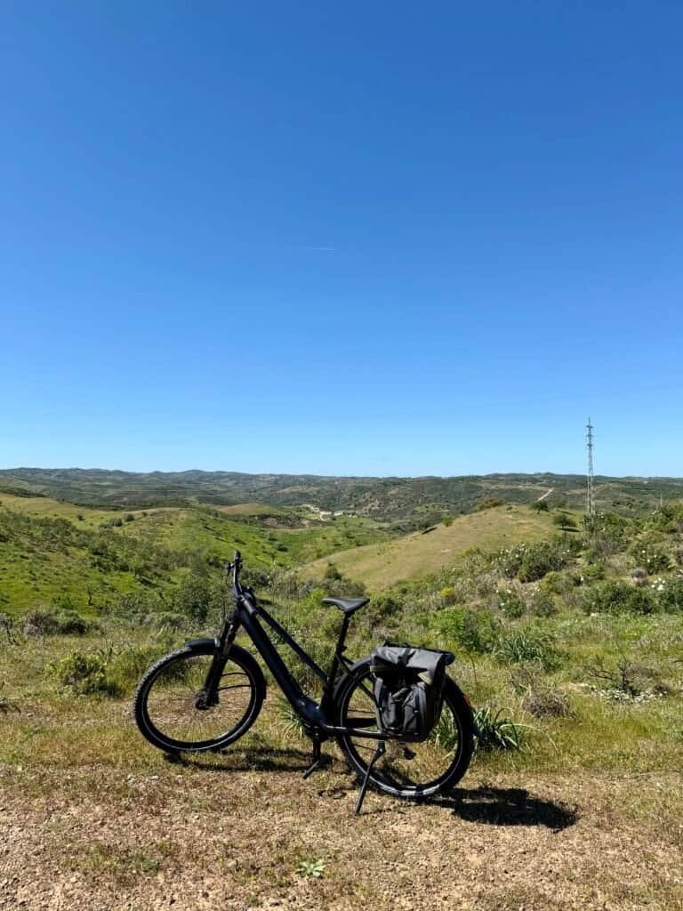 E-bike resting on scenic Algarve cycling route with rolling hills and blue sky.