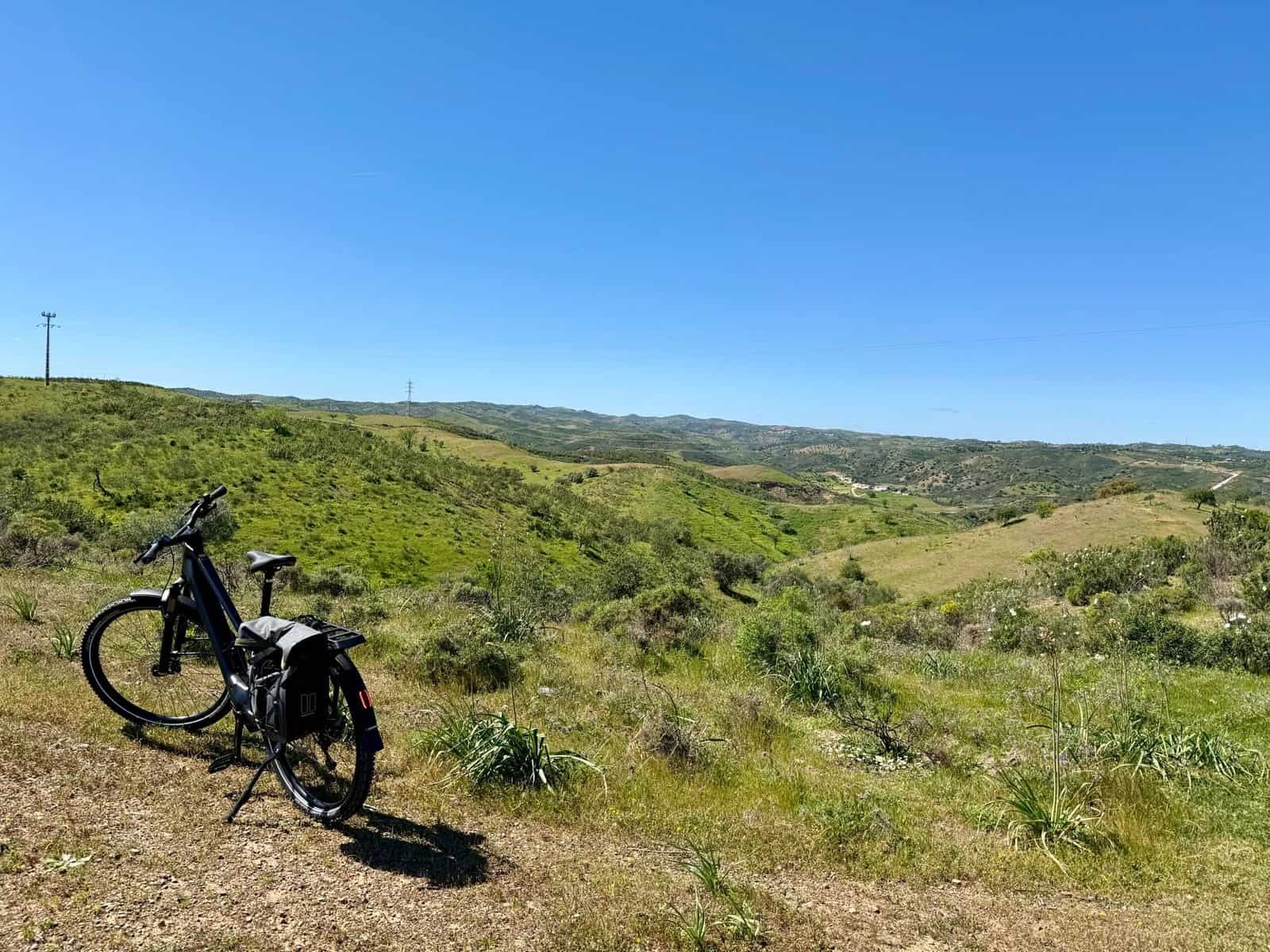 Bicycle resting on grassy terrain with expansive green hills and clear blue sky in the background.