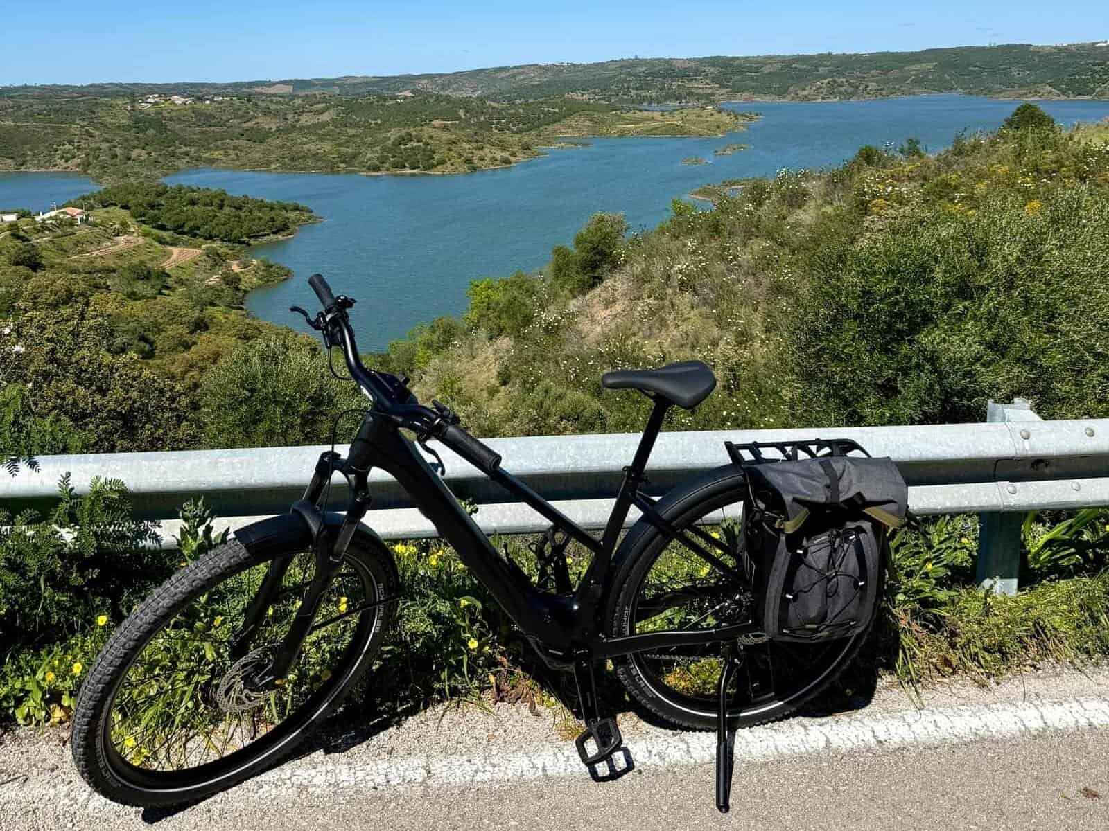 Algarve cycling ride with scenic lake view, featuring a black bicycle on a roadside overlooking lush.